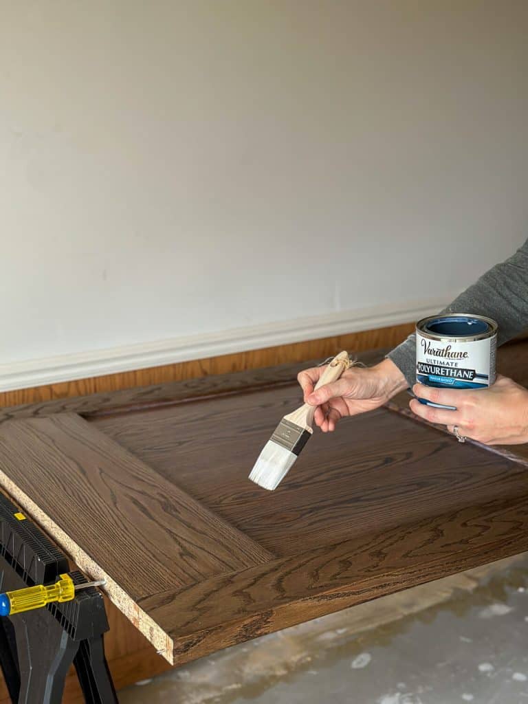 Applying polyurethane to a stained door.