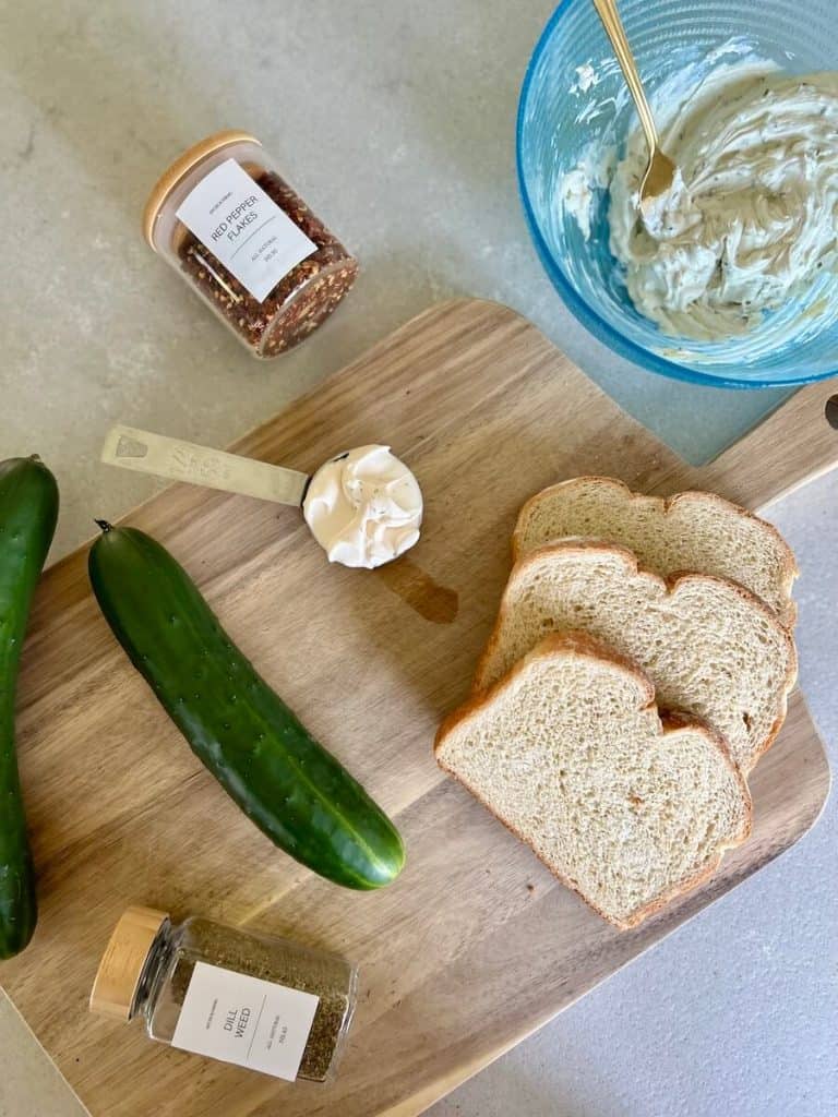 Sliced bread and a cucumber on a cutting board.